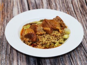 carne de cordero sobre quinoa y verduras escalibadas en un plato blanco