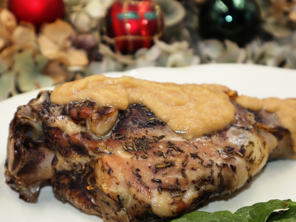 Pierna de cordero asada con salsa cremosa de manzana, servida en bandeja con bolas de Navidad de fondo.