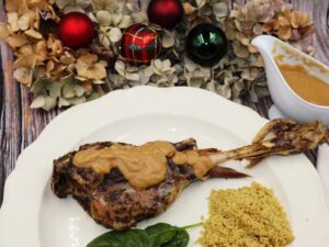 Pierna de cordero asada con salsa cremosa de manzana, servida en bandeja con bolas de Navidad de fondo.